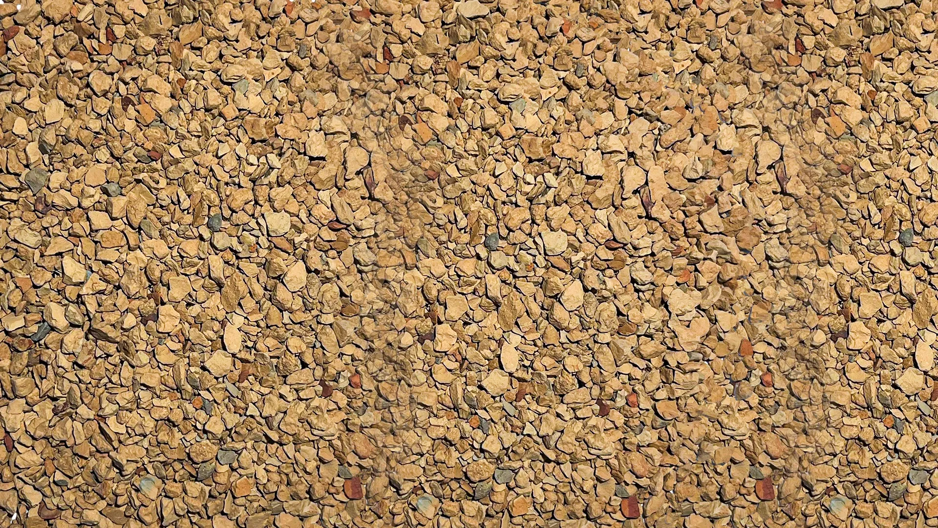 A close-up view of a surface covered with many small, irregularly shaped light brown stones or gravel, creating a rough and textured pattern.