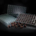 Three clear plastic seedling trays, two stacked and one upright, with brown soil plugs filling some cells. Several soil plugs are placed in front of the trays, all against a black background.