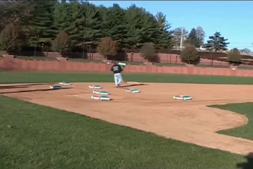 Groundskeeper applying soil conditioner across a baseball infield, with multiple bags of product spread on the dirt surface.