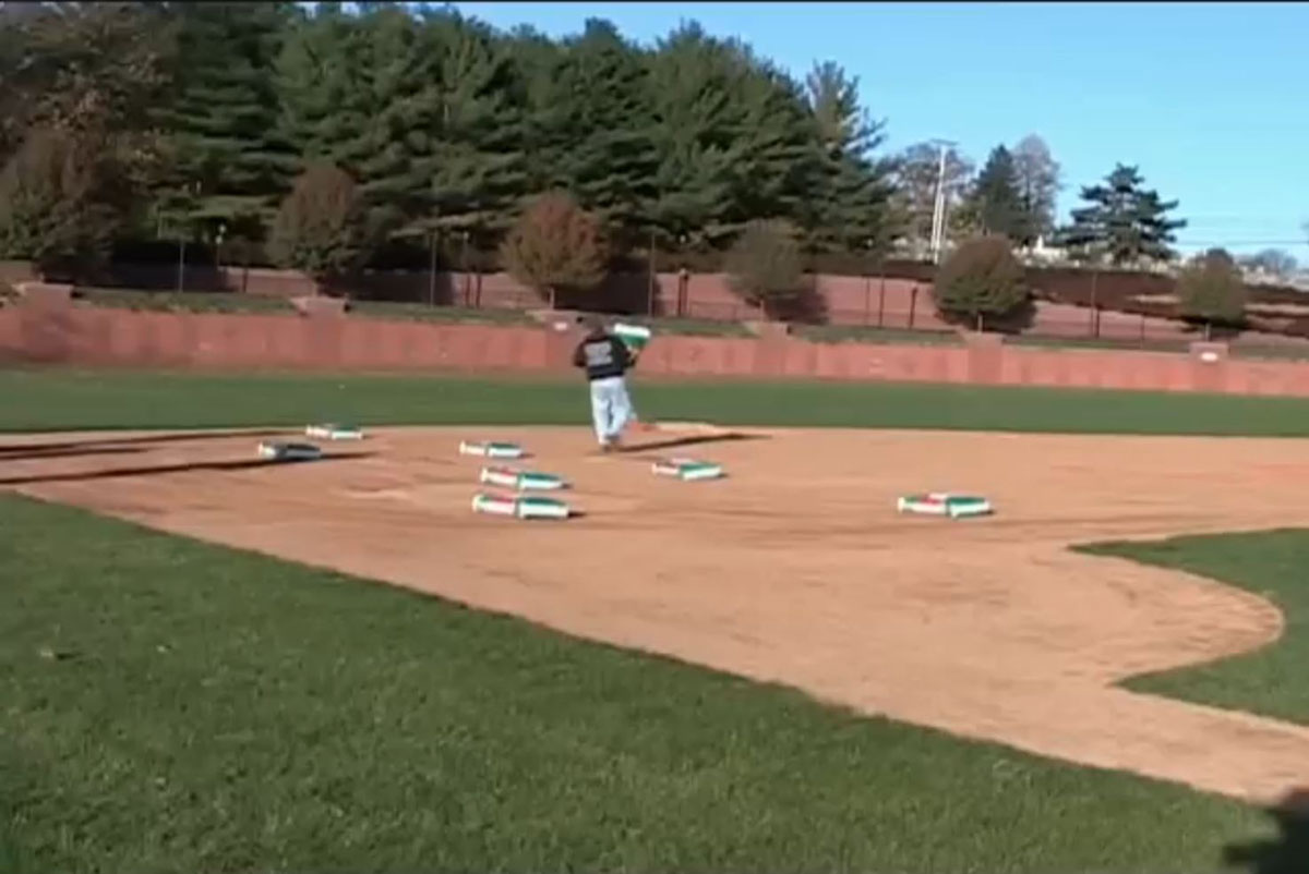 Groundskeeper applying soil conditioner across a baseball infield, with multiple bags of product spread on the dirt surface.