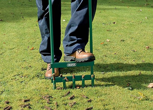 Person using a manual lawn aerator tool to remove plugs of soil from turf.