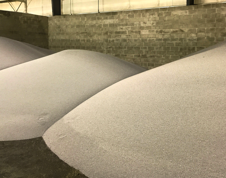 Large indoor piles of granular fertilizer material stored in a warehouse.