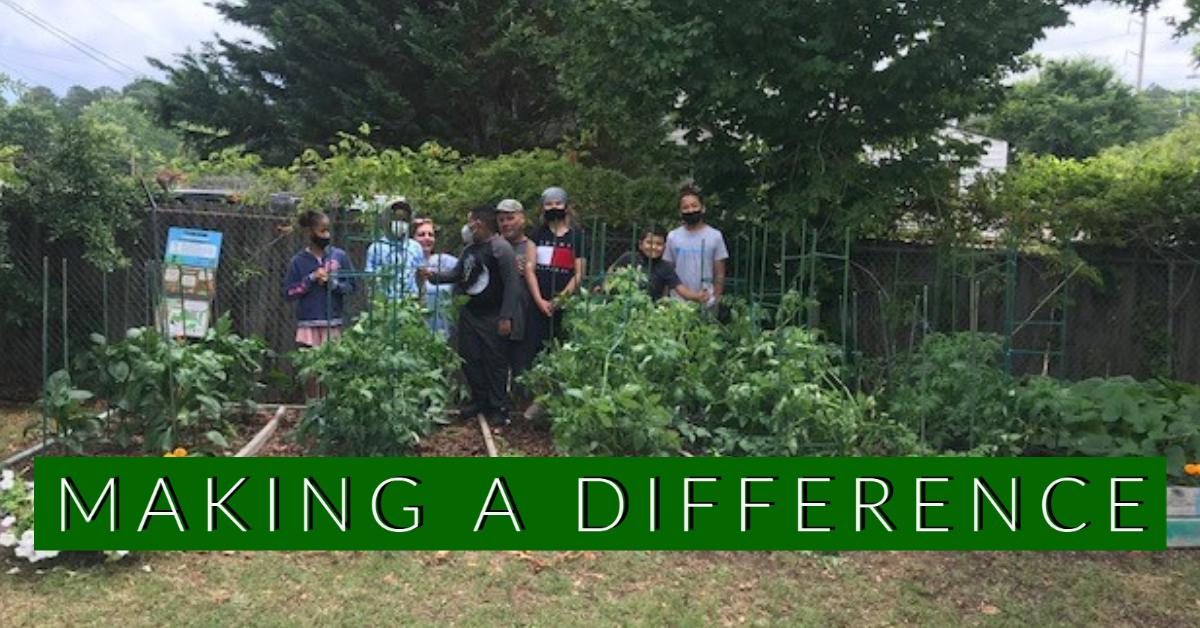 Wide view of a community garden with a group standing in the background and the words “Making a Difference” across the bottom.