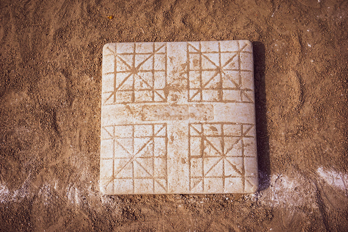 A square marble board with engraved geometric patterns sits on sandy ground, possibly used for a traditional game.