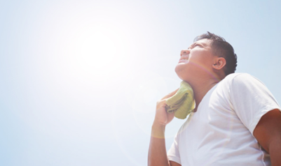 Person wiping sweat from their neck while standing in bright sunlight.