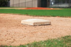 A close-up view of a base on a baseball field, with green grass and a dirt infield visible in the background.