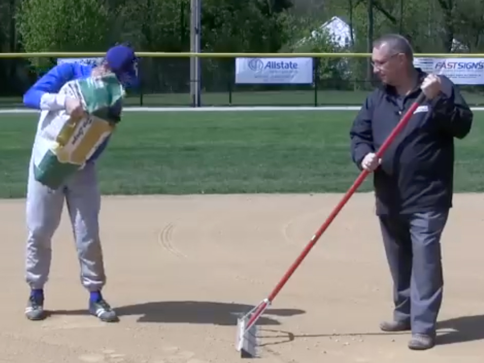 Athletic staff raking an infield.