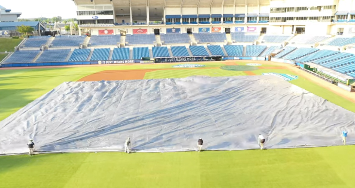 Removing a tarp from a baseball field.