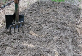 Pile of sandy soil being mixed outdoors with a pitchfork standing in the mound.