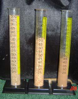 Three graduated cylinders filled with sand at different compaction levels, each marked with measurement scales for comparison.