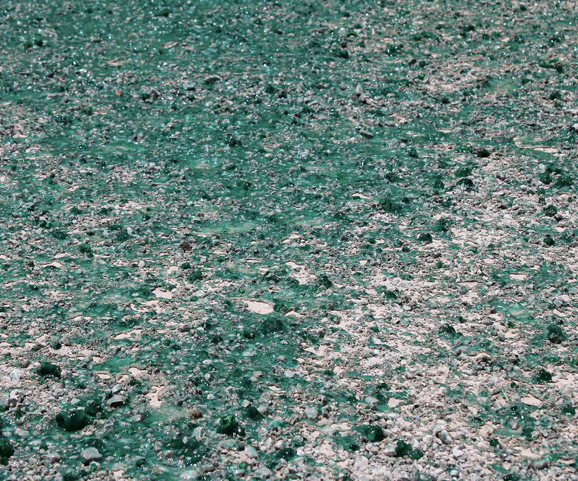 Ground covered with patches and droplets of thick green gel-like liquid mixed with gravel and dirt.