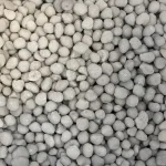 A close-up view of many small, round, light gray pebbles closely packed together, creating a textured and uniform surface.