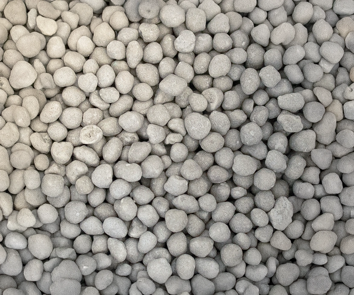 A close-up view of many small, round, light gray pebbles closely packed together, creating a textured and uniform surface.