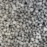A close-up view of numerous small, round, and smooth stones or pebbles in varying shades of gray, densely packed together.