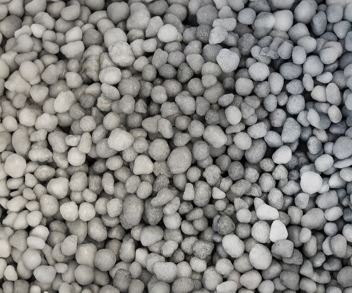 A close-up view of numerous small, round, and smooth stones or pebbles in varying shades of gray, densely packed together.