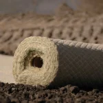 Rolled erosion control blanket made of natural fiber material resting on soil at a construction or landscaping site.
