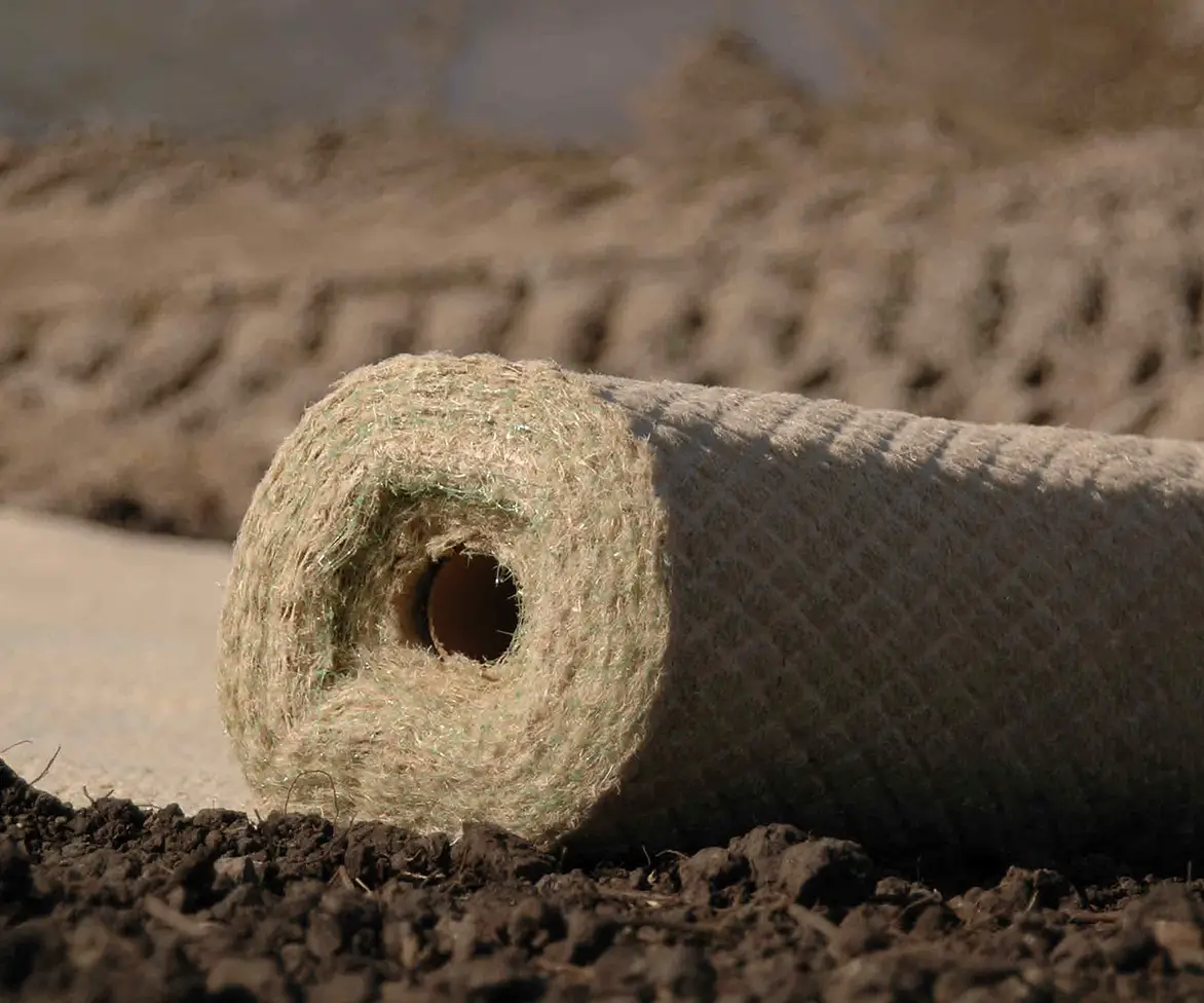 Rolled erosion control blanket made of natural fiber material resting on soil at a construction or landscaping site.