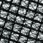 Close-up of black synthetic turf reinforcement mesh with an irregular web-like pattern forming a grid structure.