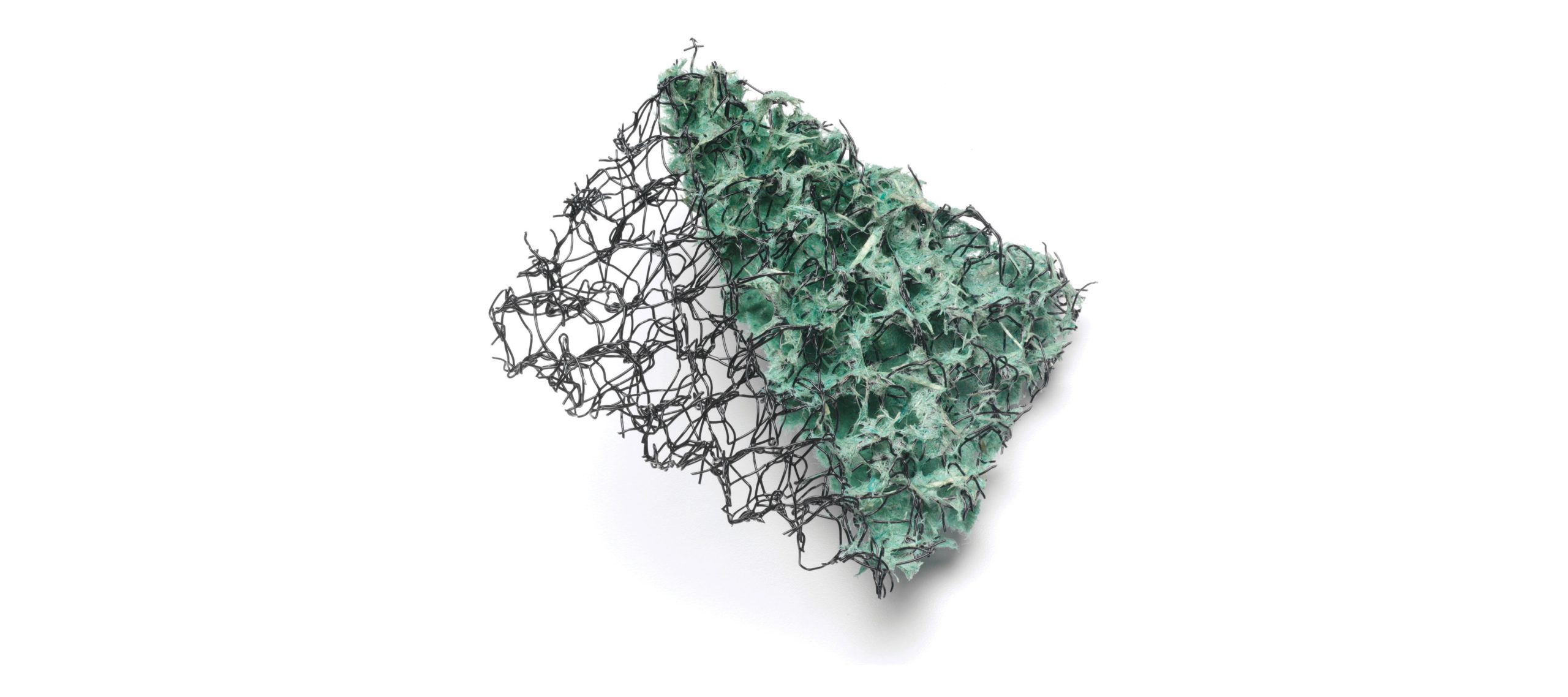 A piece of green abrasive scrubbing pad with a black plastic mesh backing, photographed on a white background.