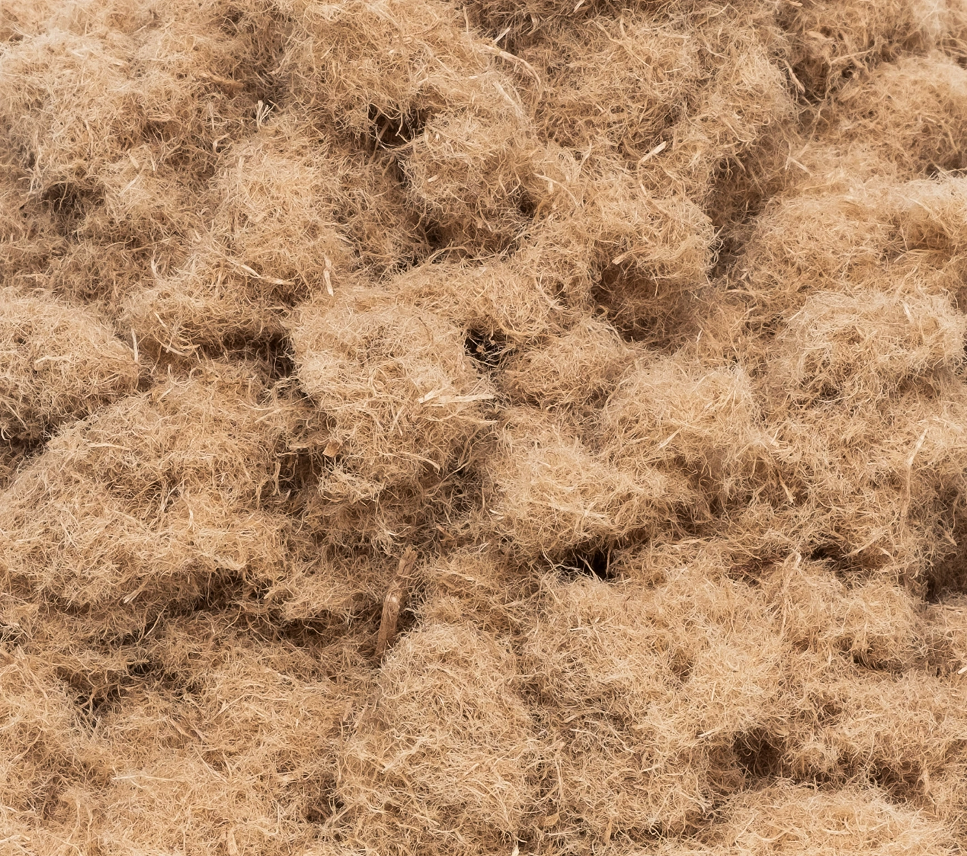 A close-up view of a pile of light brown, fibrous, and fluffy natural material, possibly coconut coir or another plant fiber used for gardening or crafts.