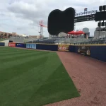 Professional baseball field with neatly maintained grass and warning track, with stadium seating and scoreboard in the background.
