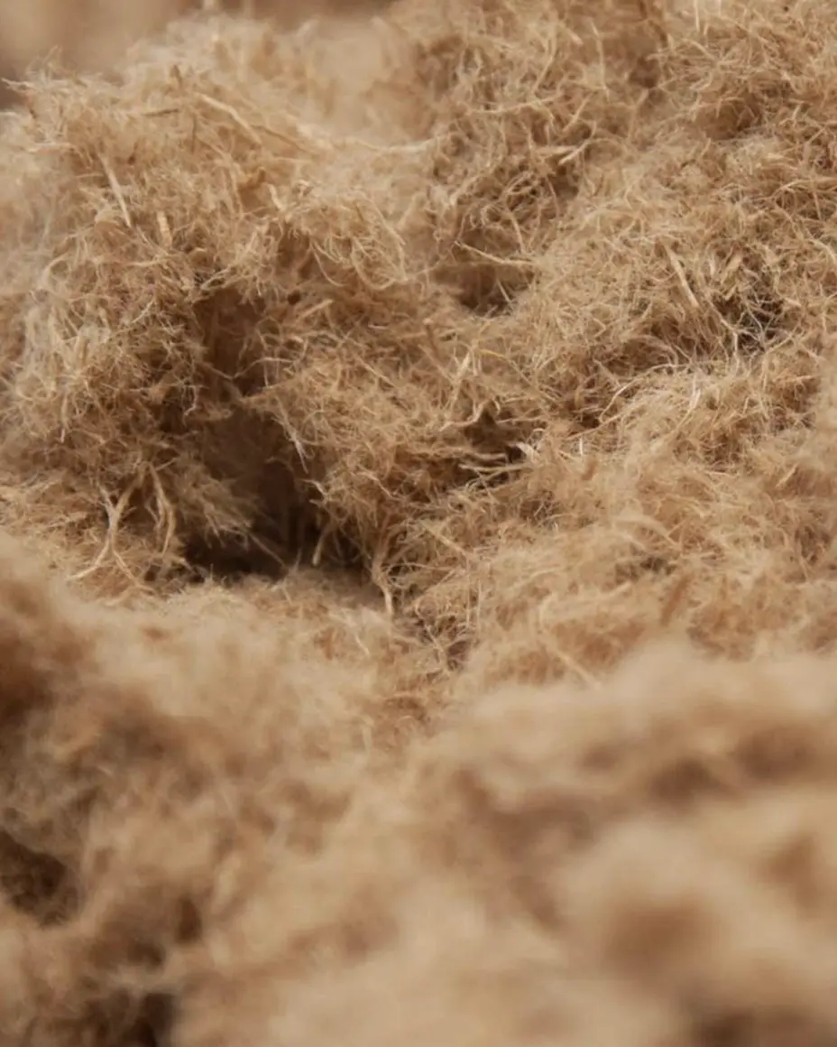 Close-up of tangled, fluffy brown fibers, resembling natural plant material or textile fibers, with a soft texture and uneven surface.