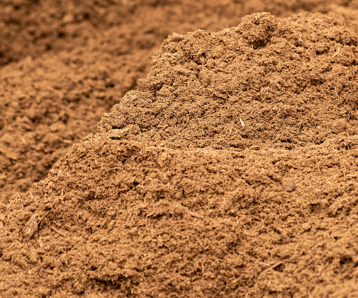 A close-up view of a large pile of loose, brown soil or mulch, with a rough and textured surface.
