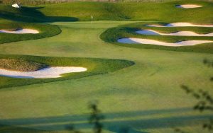 A golf course with neatly mowed grass, several sand bunkers, and a flag marking the hole in the distance under clear daylight.