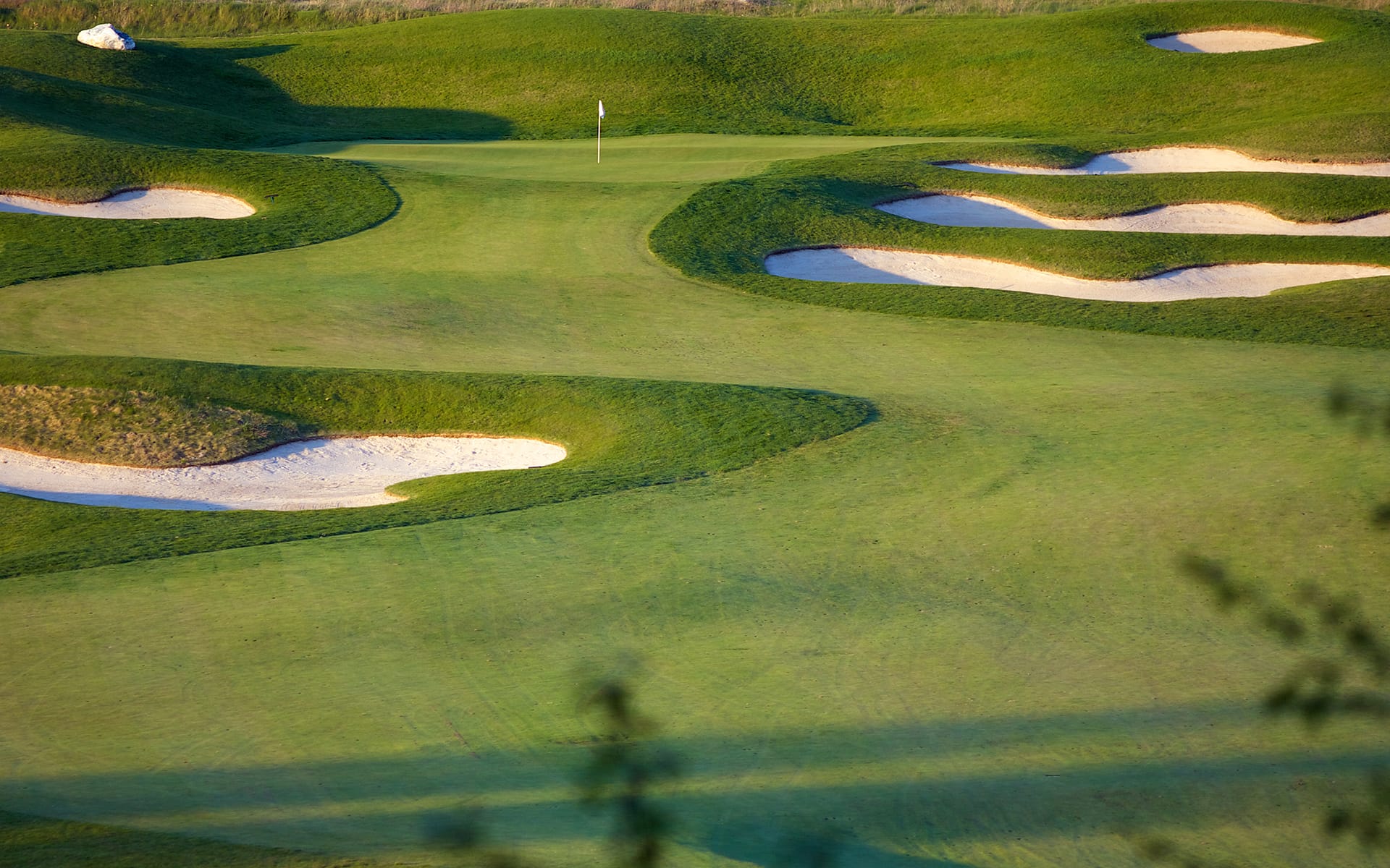 A golf course with neatly mowed grass, several sand bunkers, and a flag marking the hole in the distance under clear daylight.