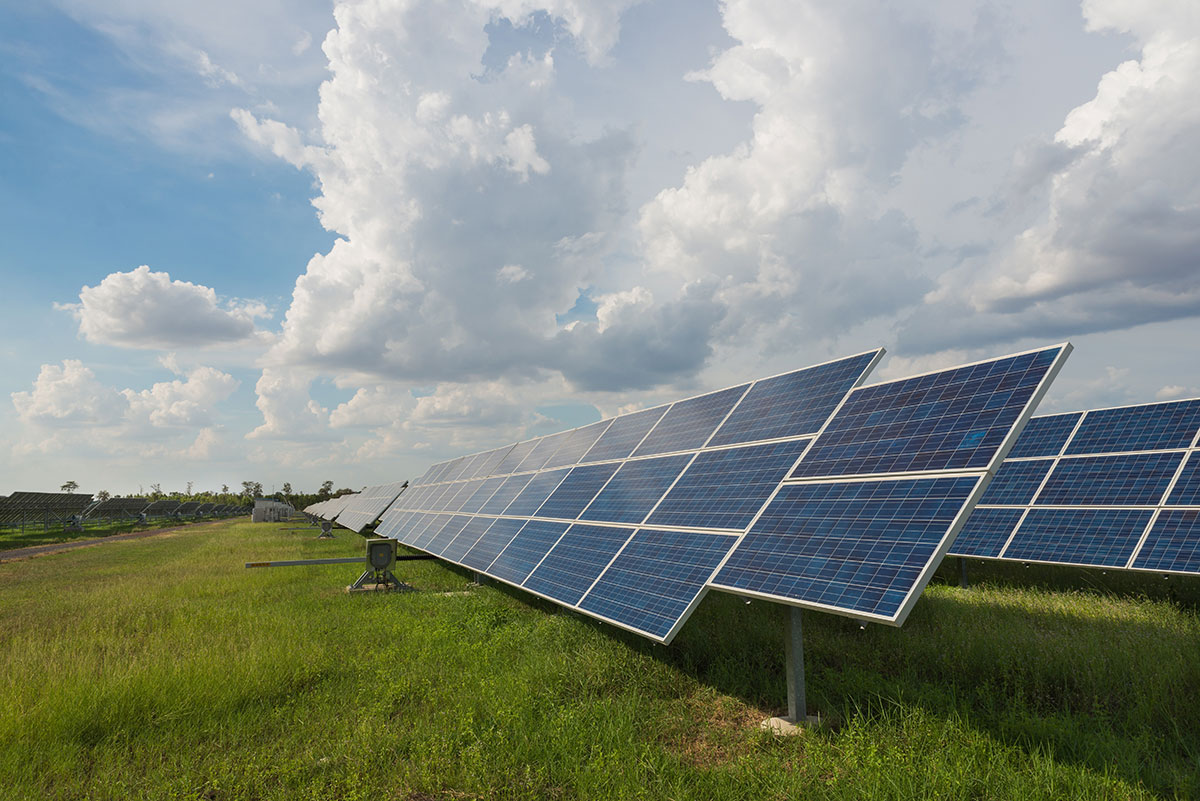 Rows of solar panels stand in a grassy field under a partly cloudy sky, capturing sunlight to generate renewable energy.