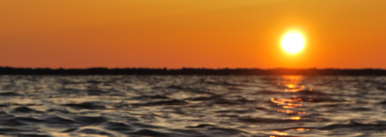 Orange sunset over a body of water with the sun near the horizon and its reflection on the waves.