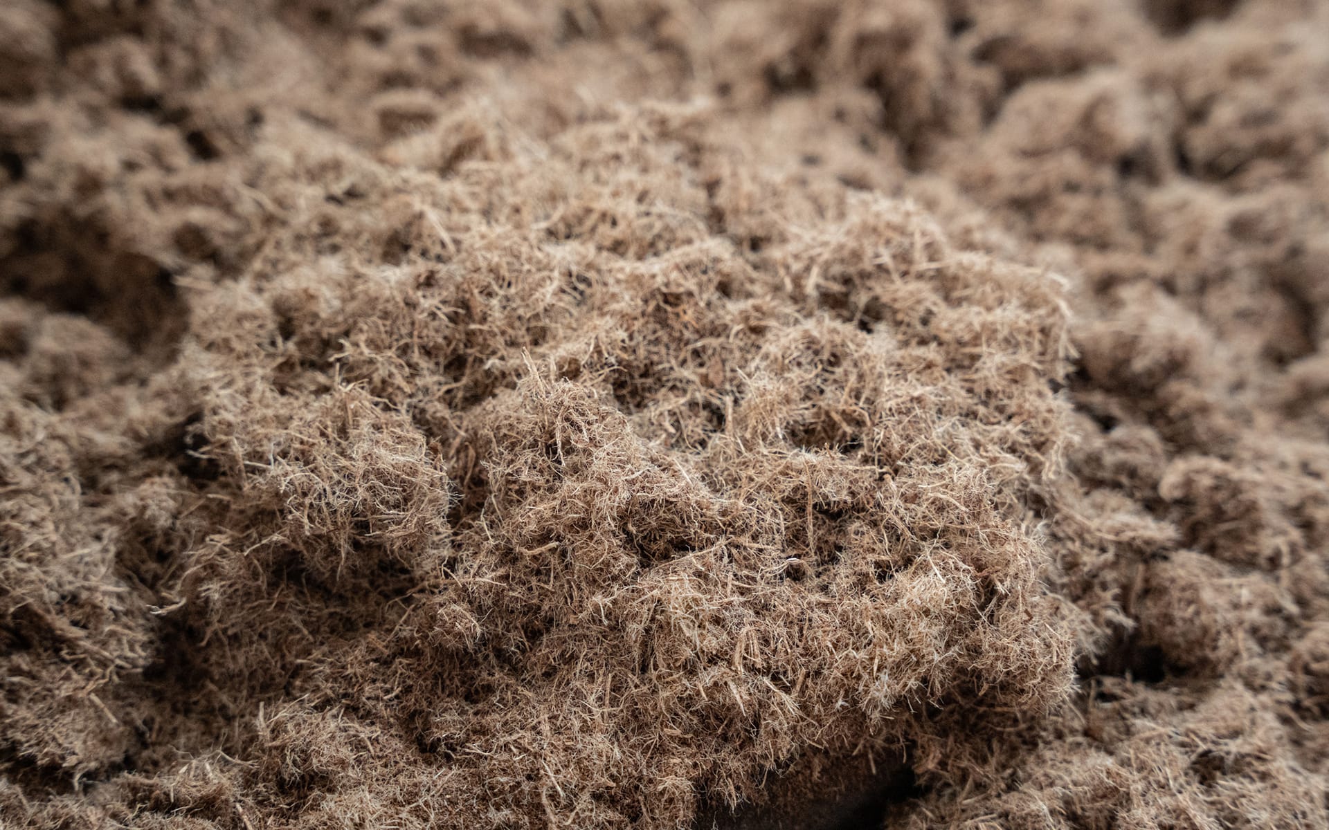 Close-up of a pile of brown, fibrous, natural material resembling coconut coir or dried plant fibers, showing a rough and textured surface.