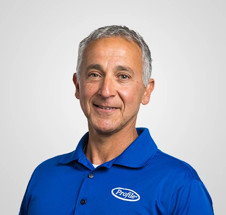 Smiling middle-aged man with short gray hair wearing a blue Profile polo shirt, posing in front of a plain light gray background.