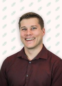 A smiling man with short light brown hair wears a maroon shirt. The background is white with a repeating green logo pattern.
