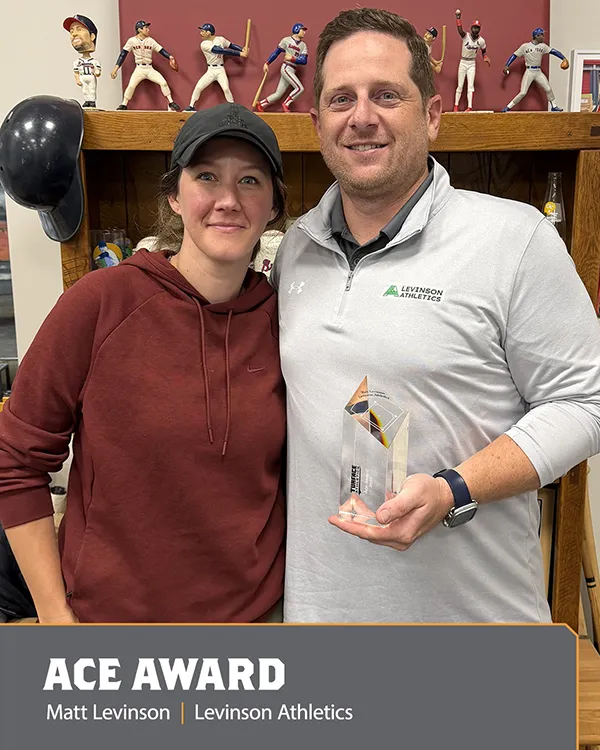 Two people stand together smiling; one holds a clear award trophy. Baseball memorabilia is displayed on the shelf behind them. Text at the bottom reads: ACE AWARD Matt Levinson | Levinson Athletics..