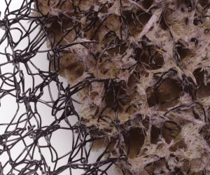 A close-up of a textured surface with tangled black wires and fibrous brown and pinkish materials, creating an intricate and abstract pattern.