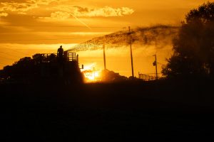 Silhouette of a person on a machine spraying water at sunset with orange sky and trees. Hydroseeding application on a data center project site, providing erosion control protection until natural vegetation is established.