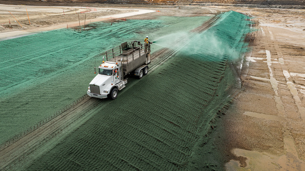A truck sprays green hydroseed on a sloped dirt surface at a construction or mining site, utilizing hydromulching to promote rapid vegetation growth and soil stabilization.